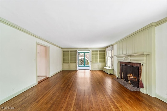 unfurnished living room featuring baseboards, ornamental molding, wood finished floors, built in shelves, and a fireplace