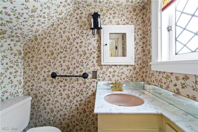 half bathroom with toilet, wallpapered walls, and vanity