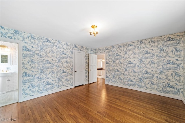 empty room featuring wallpapered walls, baseboards, and wood finished floors