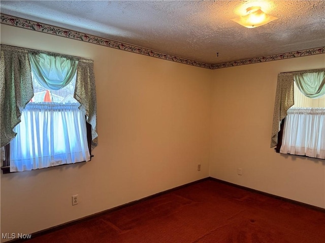 spare room with a textured ceiling, dark carpet, and baseboards