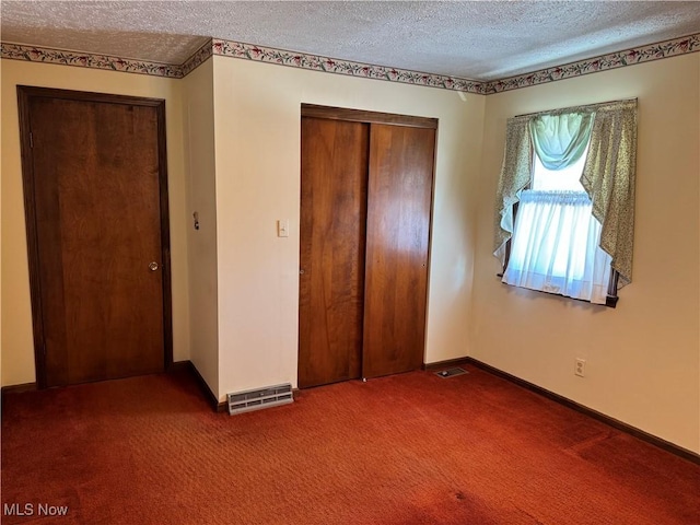 unfurnished bedroom featuring dark colored carpet, a closet, visible vents, a textured ceiling, and baseboards