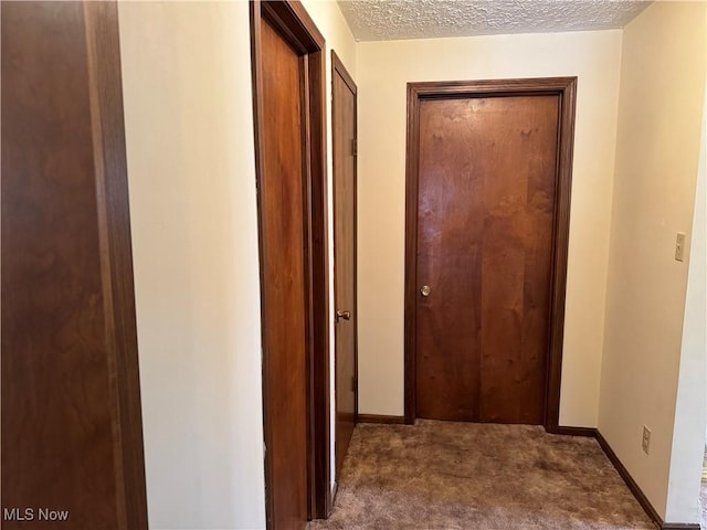 hallway with baseboards, dark carpet, and a textured ceiling