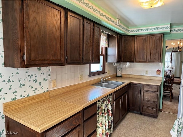 kitchen with tasteful backsplash, light countertops, a sink, dark brown cabinetry, and wallpapered walls