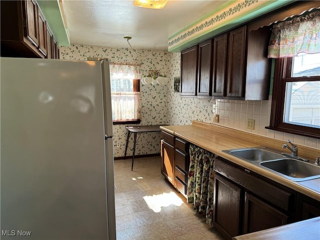 kitchen with pendant lighting, freestanding refrigerator, a sink, dark brown cabinetry, and wallpapered walls