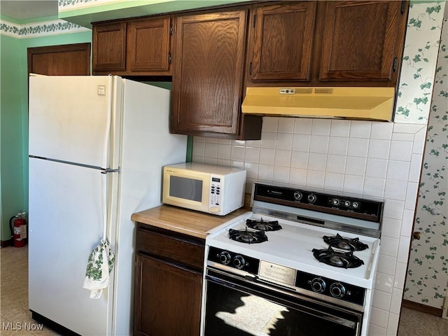 kitchen featuring exhaust hood, light countertops, decorative backsplash, white appliances, and wallpapered walls