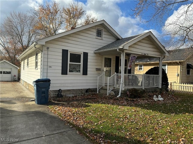 bungalow-style house with a shingled roof, a front yard, an outdoor structure, and a detached garage