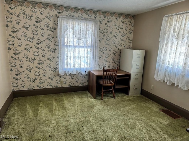 carpeted home office featuring wallpapered walls, baseboards, and visible vents