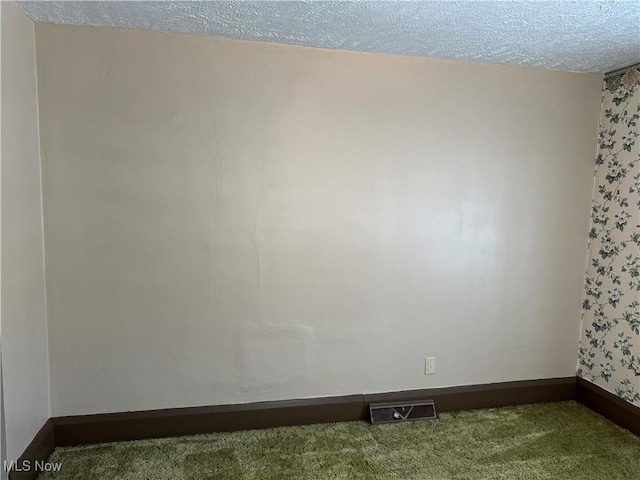 unfurnished room with a textured ceiling, carpet flooring, visible vents, and baseboards