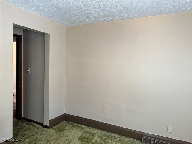 spare room with dark colored carpet, a textured ceiling, and baseboards