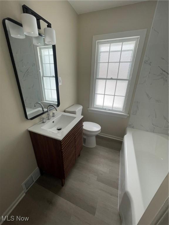 full bath featuring baseboards, visible vents, toilet, a bathing tub, and vanity