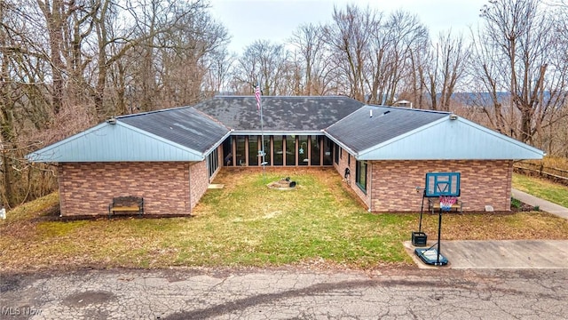 view of front of home with brick siding, a front yard, and a sunroom