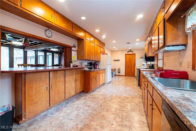 kitchen with black dishwasher, stainless steel range, brown cabinetry, and freestanding refrigerator