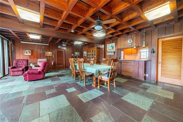 dining space featuring ceiling fan, wooden walls, coffered ceiling, and stone tile flooring