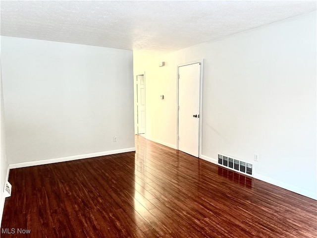 unfurnished room featuring a textured ceiling, dark wood-type flooring, visible vents, and baseboards