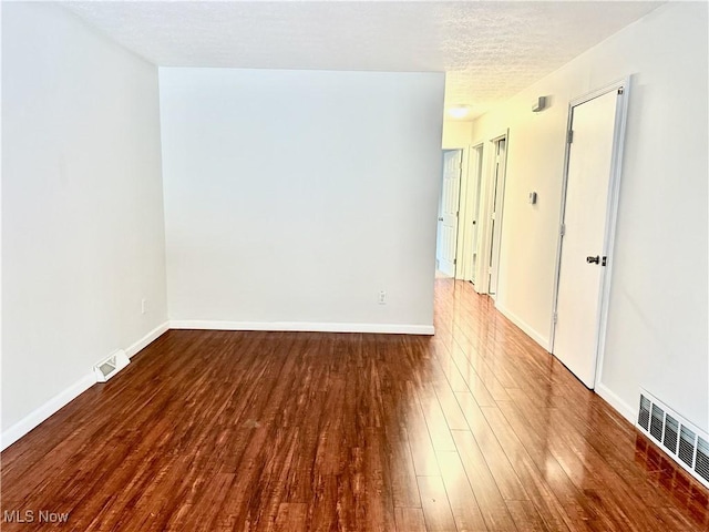 unfurnished room with a textured ceiling, wood finished floors, visible vents, and baseboards