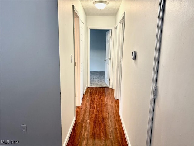 hallway featuring a textured ceiling, dark wood-style flooring, and baseboards