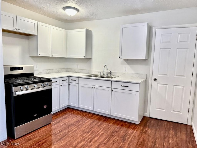 kitchen with a textured ceiling, dark wood-style flooring, a sink, white cabinetry, and stainless steel gas stove