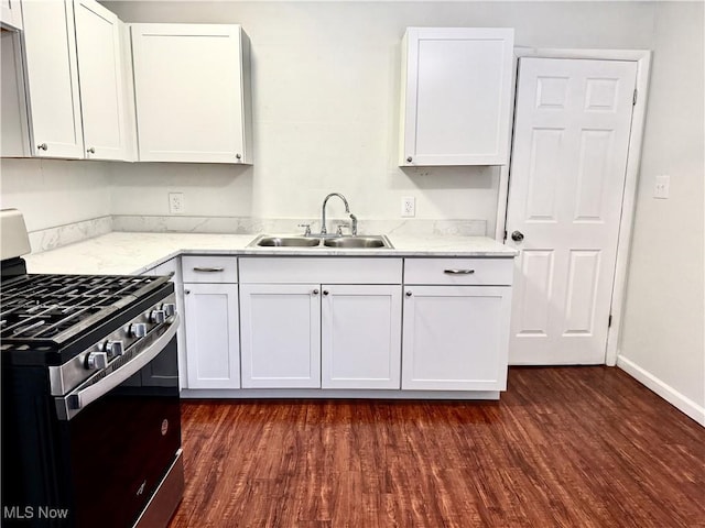 kitchen with dark wood finished floors, white cabinets, gas range, light stone countertops, and a sink