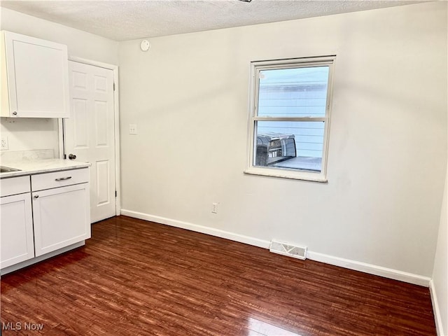 unfurnished dining area featuring dark wood-style floors, visible vents, and baseboards