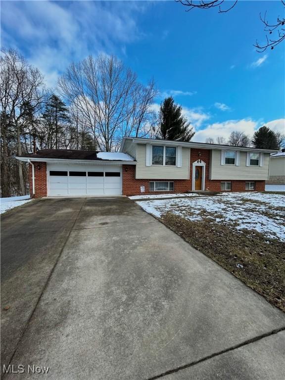 raised ranch with a garage, concrete driveway, and brick siding