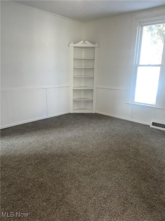 empty room with carpet floors, wainscoting, and crown molding