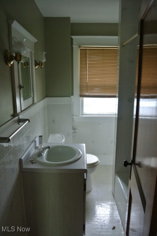 bathroom featuring tile walls, wainscoting, vanity, and toilet