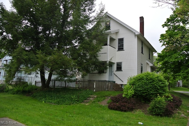 view of side of home with entry steps, a yard, a chimney, and fence