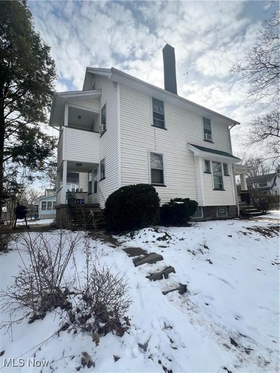 snow covered house featuring a chimney and a porch