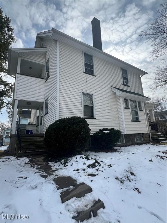 snow covered back of property with covered porch and a chimney