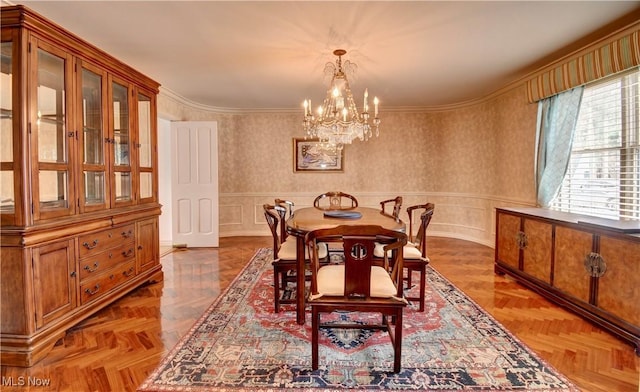 dining room featuring wallpapered walls, wainscoting, ornamental molding, a decorative wall, and a notable chandelier