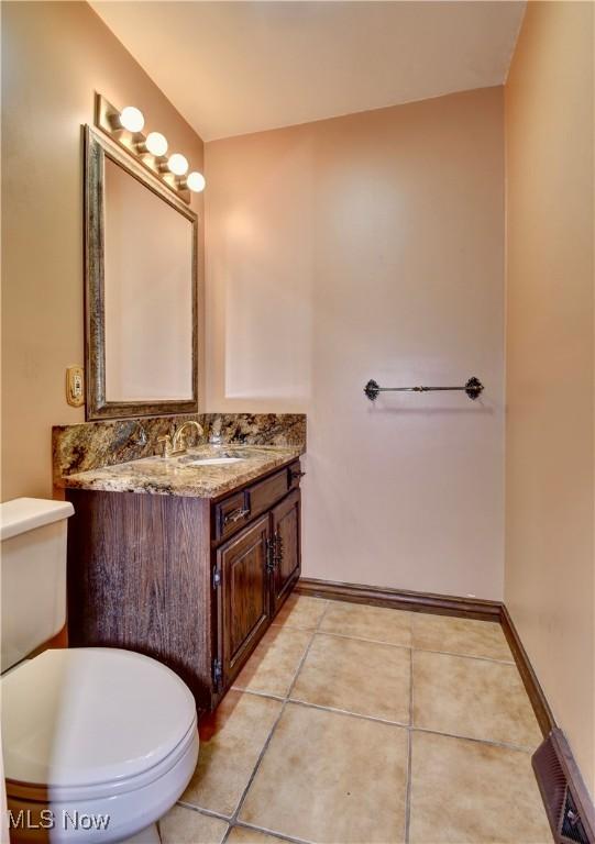 half bathroom with toilet, vanity, visible vents, baseboards, and tile patterned floors