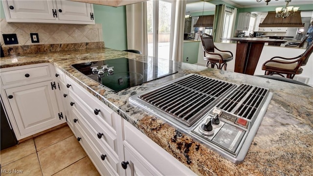 kitchen featuring stainless steel gas cooktop, light stone counters, black electric stovetop, and white cabinetry