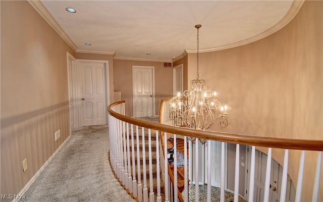 hallway featuring a chandelier, carpet floors, visible vents, baseboards, and ornamental molding