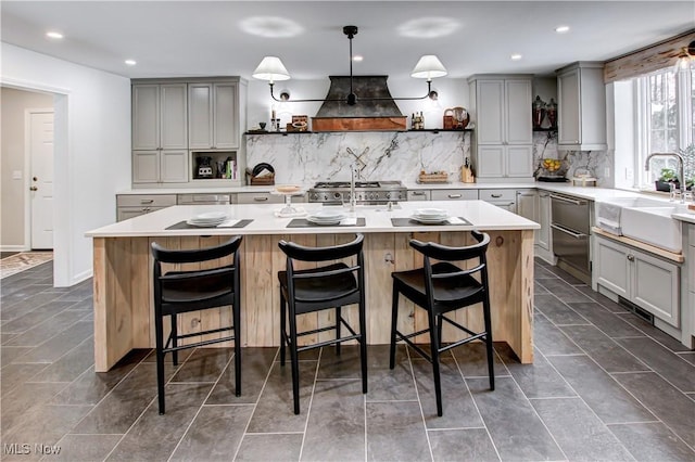 kitchen featuring a breakfast bar, a kitchen island with sink, custom exhaust hood, and light countertops