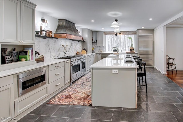 kitchen with a breakfast bar, light countertops, a kitchen island, built in appliances, and premium range hood