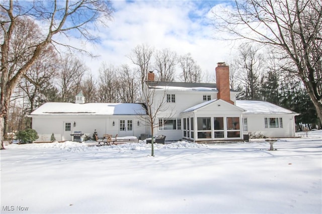 snow covered property with a chimney and a sunroom