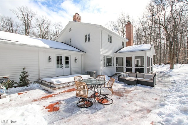 snow covered rear of property with a sunroom, a chimney, and central AC unit