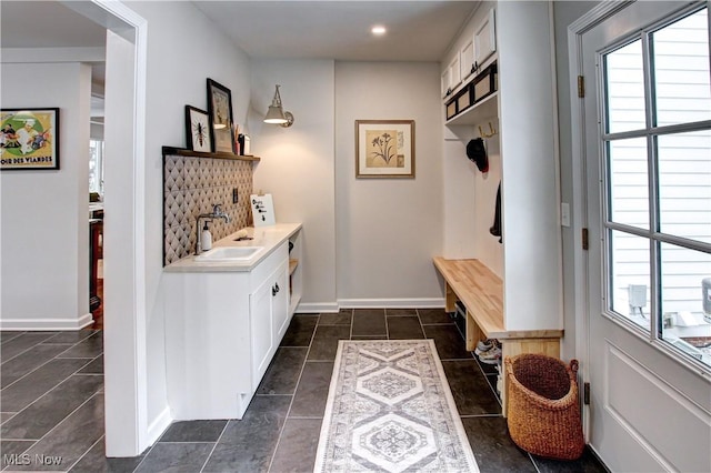 mudroom with baseboards, dark tile patterned flooring, a sink, and a healthy amount of sunlight