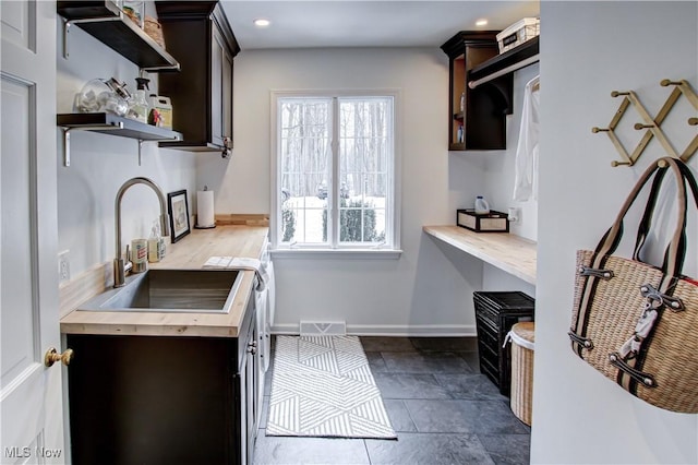 kitchen with dark brown cabinetry, visible vents, open shelves, and a sink