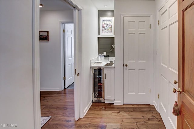 hallway featuring wine cooler, a sink, and wood finished floors