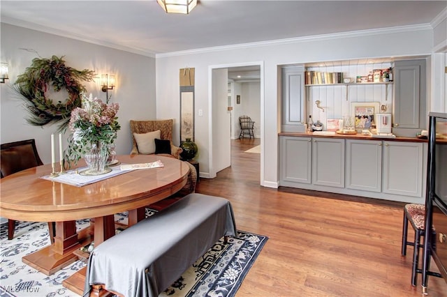 dining area featuring ornamental molding, light wood-style flooring, and baseboards