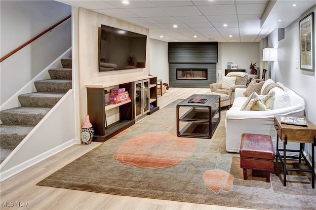 living room featuring a drop ceiling, light wood-style flooring, recessed lighting, a fireplace, and stairway