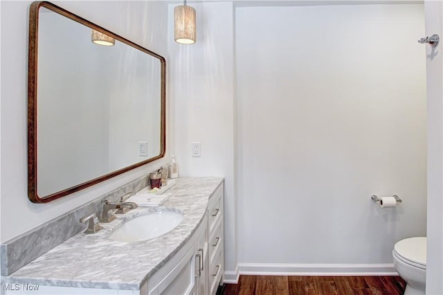 bathroom featuring toilet, baseboards, wood finished floors, and vanity