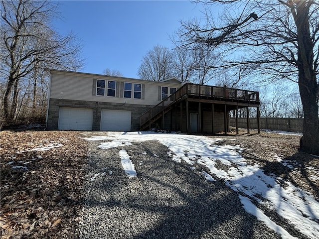 view of front of house featuring driveway, stone siding, an attached garage, stairs, and a deck