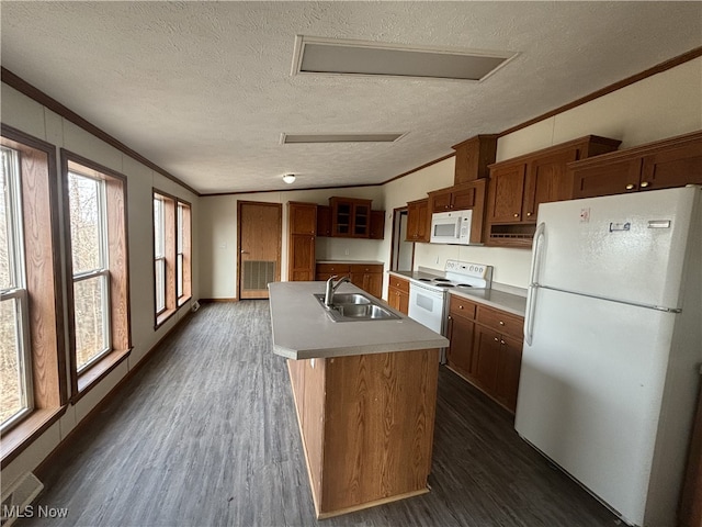 kitchen featuring ornamental molding, white appliances, a kitchen island with sink, and a sink