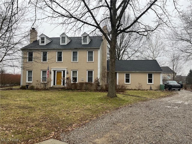 colonial home featuring a front lawn, a chimney, and brick siding