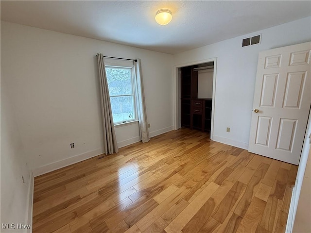 unfurnished bedroom featuring light wood-type flooring, baseboards, visible vents, and a closet