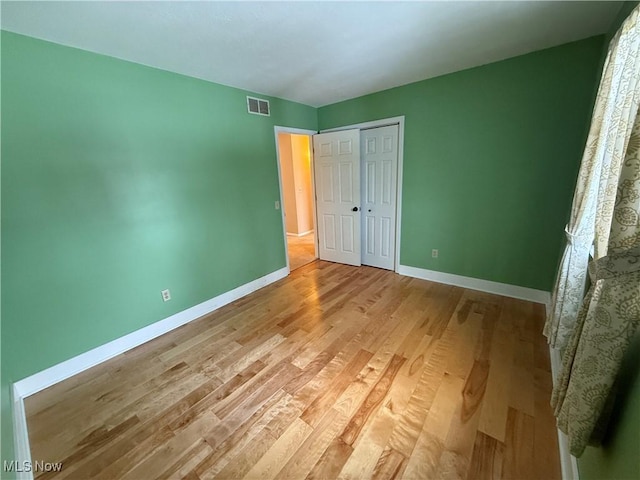 unfurnished bedroom featuring a closet, baseboards, visible vents, and light wood finished floors