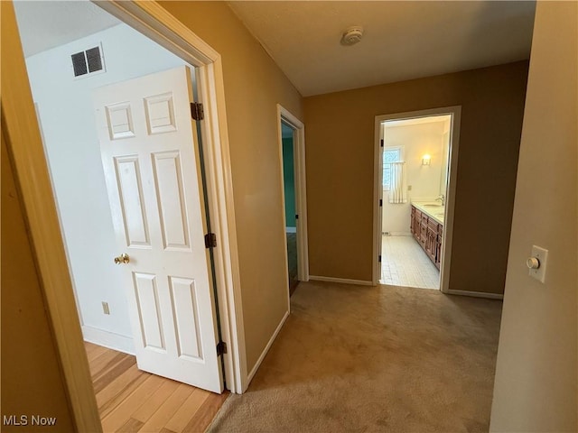 hall featuring light carpet, visible vents, and baseboards