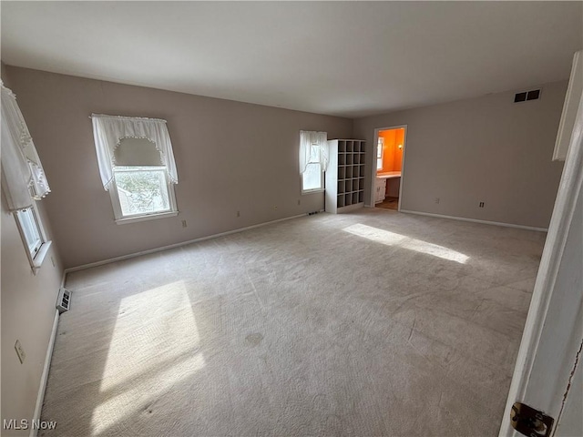 spare room featuring light colored carpet, visible vents, and baseboards